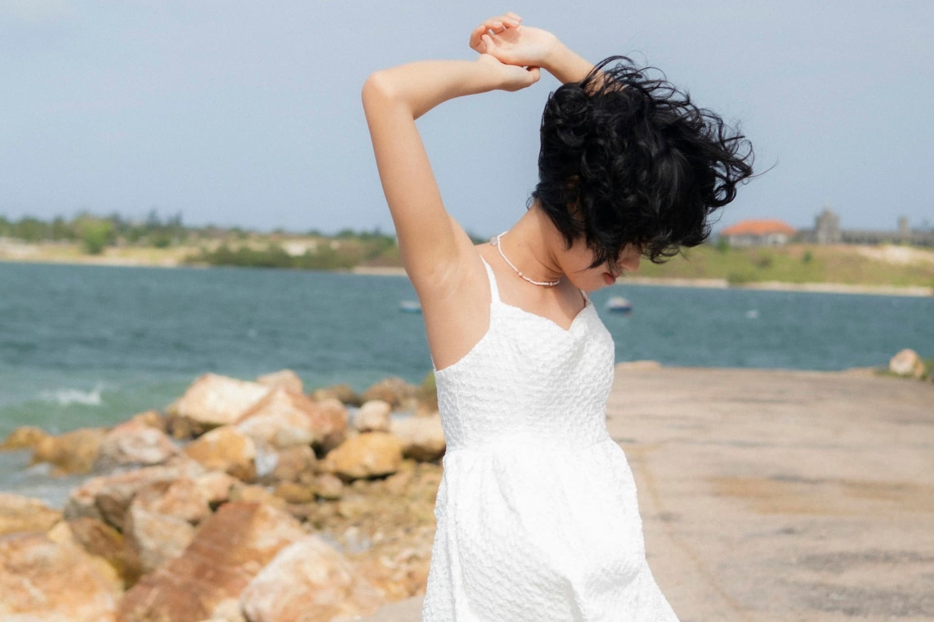 A woman in a flowing white dress walks along a quiet sandy beach in soft natural light